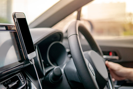 Male driver hand holding on steering wheel using smartphone for GPS navigation. Mobile phone mounting with magnet on the car console in modern car. Urban driving lifestyle with mobile app technology