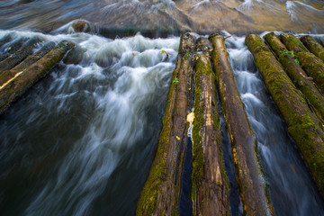 The river stream flows through the wooden log flooring. Waterfall and jets of water.