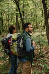 side view of man and woman with backpacks hiking in woods together