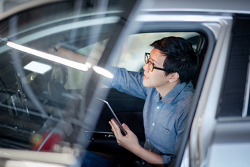 Young Asian businessman with glasses using digital tablet turning on the light while sitting on driver seat in his car. Business and transportation technology concept