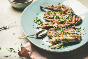Meat dinner. Grilled lamb ribs with green parsley and sauce in blue serving plate over concrete table background, selective focus, horizontal composition. Slow comfort food concept