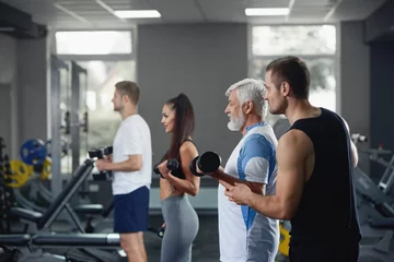 Stoff pro Meter Elderly man doing exercise with group of younger people at gym. © serhiibobyk