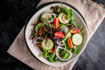 Close up vegetable salad with fresh lettuce, tomatoes and cucumber in white plate on black background