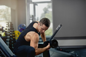Fototapeta na wymiar Handsome sporty man flexing muscles with barbell in dark gym.