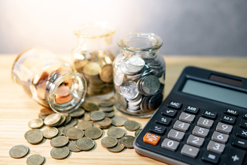 Calculator with coin in currency glass jar and spilling on wooden table. Compound interest rate...