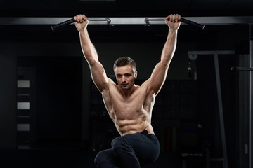 Fototapeta na wymiar Muscular male athlete pulling up on horizontal bar in dark gym.