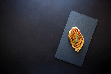Grilled chicken fillets on slate plate with rosemary, pepper and spices on dark wooden background. Top view. Flat lay. Copy space