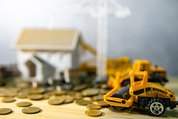 Roller truck and house models with gold coins spilling on wooden table. Real estate development or...