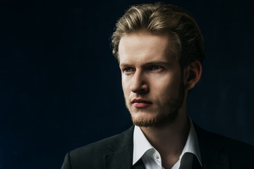 Close up studio portrait of young confident handsome man, businessman wearing classic white shirt, black jacket, posing on dark background. Copy, empty space for text