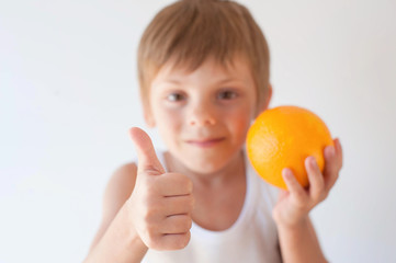 healthy small caucasian kid in white shirt holding orange and showing thumb up