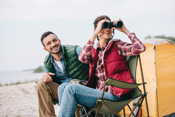 Fototapeta premium couple with binoculars resting on chairs on camping