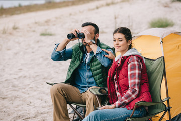 couple with binoculars resting on chairs on camping