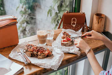 Kyiv, Ukraine - September 15, 2018: Breakfast at cafe. Toast with figs and maple syrup and toast with prosciutto and mozzarella on the table with cutlery, cup of cold ice latte and brown sparkle bag.