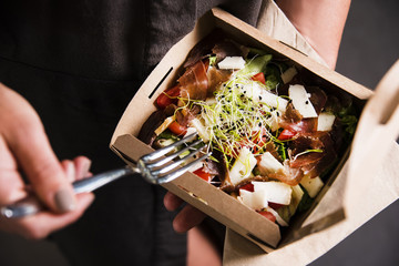 Woman's hand is holding a take away fresh salad in a lunch box. Gourmet conception. - obrazy, fototapety, plakaty