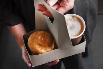 Woman is holding a take away card-box basket with coffee and cake. Food and drink conception.