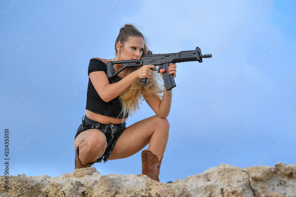 Wall mural Beautiful girl with a gun machine stands on the ruins of an ancient city