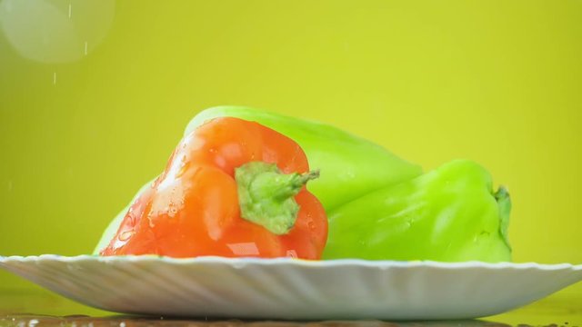 Fresh Balgar peppers fall with water on a plate. The concept of nutrition. Isolate on a yellow background, slowdown.