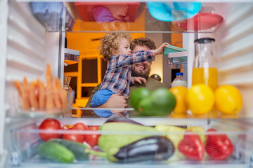 Father and son taking food from fridge late at night. Picture taken from inside of fridge.