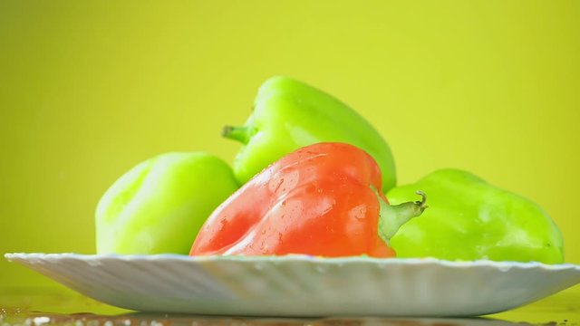 Fresh Balgar peppers fall with water on a plate. The concept of nutrition. Isolate on a yellow background, slowdown.