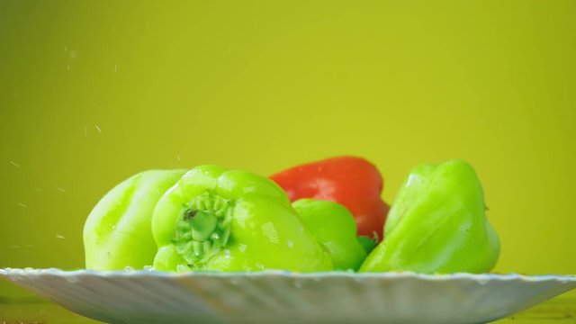 Fresh Balgar peppers fall with water on a plate. The concept of nutrition. Isolate on a yellow background, slowdown.