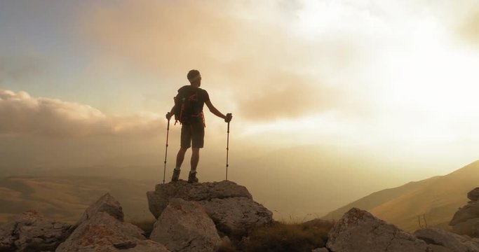 Young man hiker standing on ridge edge of the mountain in Abruzzo Italy with poles at sunset epic shot