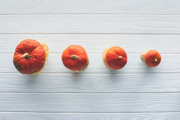elevated view of small orange autumnal pumpkins in row on wooden tabletop