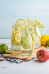 Green and yellow lemon with  green and red apples in soda bottles on cutting bord and white table