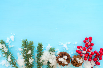 Christmas and New year background.  Fir leaves, pine cones and red berry on blue  wood table with snow. Creative flat lay , top view