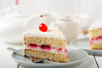 Slice vanilla cake with butter cream icing in the plate on white wooden table.