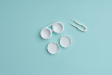 top view of white contact lenses container and tweezers on blue background