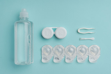 flat lay with sterile liquid in bottle, tweezers and containers for contact lenses on blue tabletop