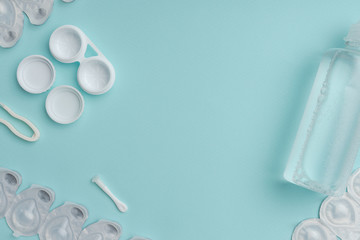 flat lay with sterile liquid in bottle, tweezers and containers for contact lenses on blue tabletop