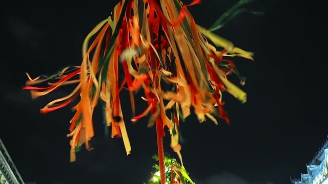 Festive Wooden Pole for Climb on Maslenitsa. Bright ribbons fluttering in the wind dark sky background. Christmastide Holiday. Camera moving up