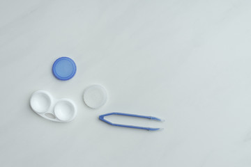 top view of contact lenses container and tweezers on white backdrop