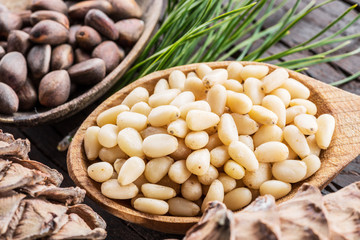 Pine nuts in the spoon and pine nut cone on the wooden table. Organic food.