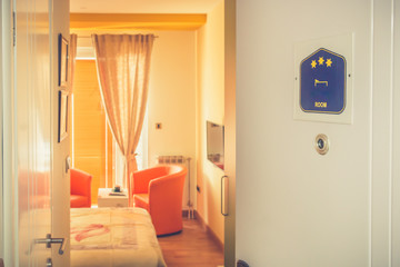 Half open door of hotel room with three stars and blurred interior of the bedroom. Close up.