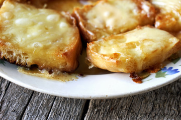 Toasts with melted cheese in an old plate on wooden boards