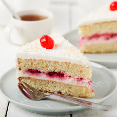 Slice vanilla cake with butter cream icing in the plate on white wooden table.