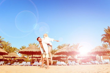  Beautiful young couple having vacation on a sunny beach walking while holding hands, hugging, and taking selfies.  Happy handsome man and blonde woman in white shirts enjoying their trip to hawaii. © Антон Зимин