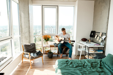 young man playing acoustic guitar at home