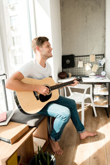 young smiling man playing acoustic guitar at home
