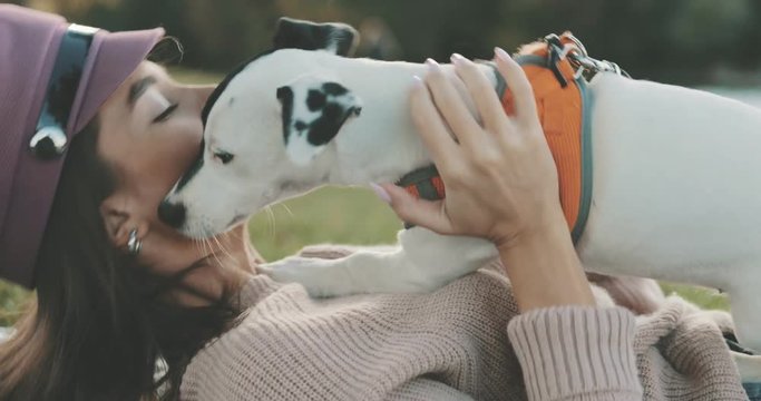 Portrait of beautiful young woman playing with dog jack russell terrier on the lake shore. A girl kissing a cute puppy. 4K video shooting