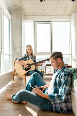 Fototapeta premium young man using digital tablet while girlfriend playing acoustic guitar at home