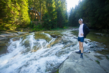 Young man walk near fast river in middle of forest