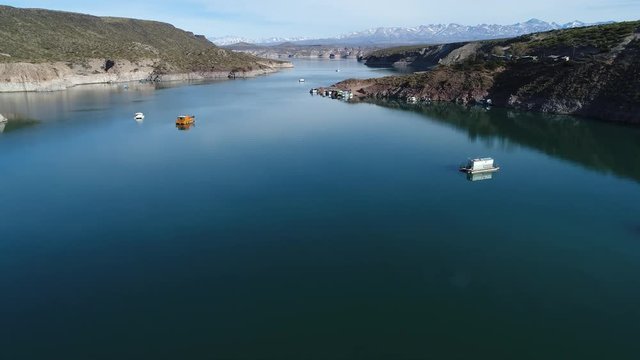 Aerial drone scene of Agua de Toro dam. Flying ascending over the lake, passing near boats. Snowy plata mountains at background. San Rafael, Mendoza, Cuyo Argentina.