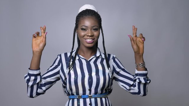 pretty african woman crossing her fingers for luck at the camera on gray background