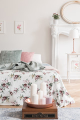English style bedroom interior with a bed dressed in rose pattern bedding and green, pink and white cushions. Candles on the floor in front of the bed. Real photo.