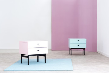 Pastel pink and baby blue night stands with drawers and black elements in a white room interior...