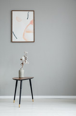 Poster on grey wall in minimal living room interior with white flowers on wooden table. Real photo