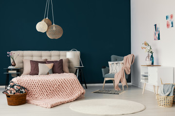 Grey armchair with powder pink blanket and cushion standing in the corner of white and blue bedroom...